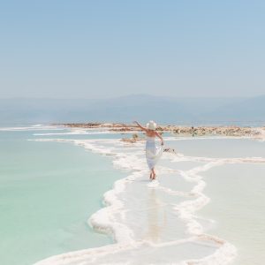 Lady Walking on a white sand beach with bare feet and blue sky and sea.