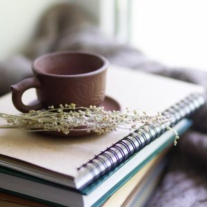 Brown tea cup on a stack of note books with a dried flower on the saucer.